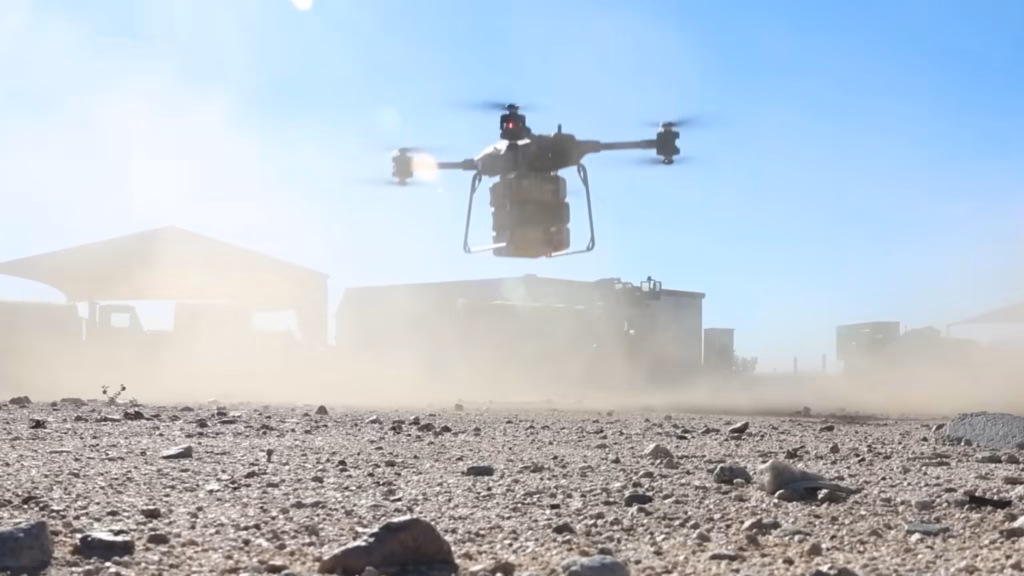 Heavy lift quadcopter drone rising above a dusty ground while carrying a payload during a test flight.